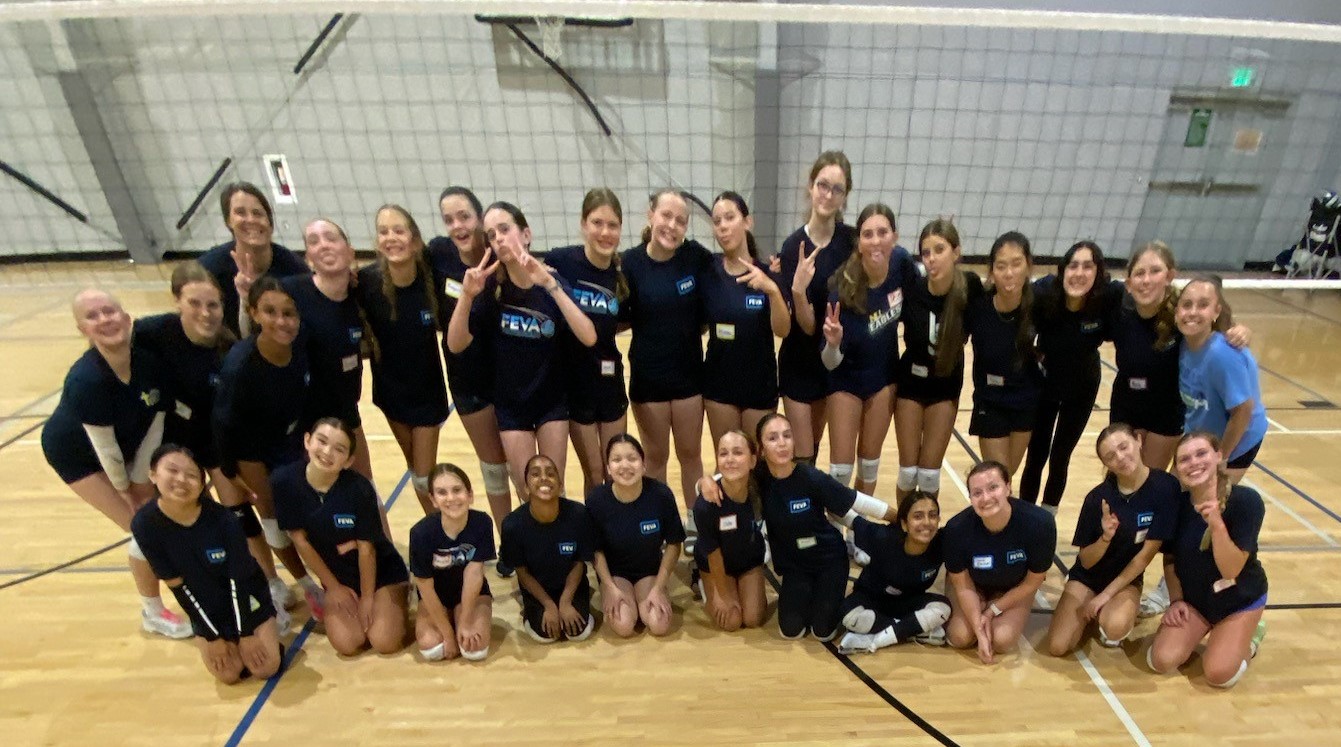 Group photo of FEVA volleyball athletes posing together in the gym, wearing matching team shirts.