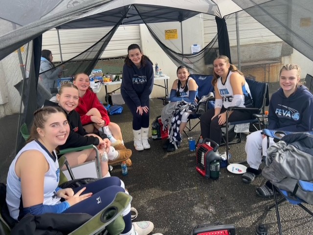 FEVA 14 volleyball team members sitting together under a tent, smiling and enjoying their time between matches.
