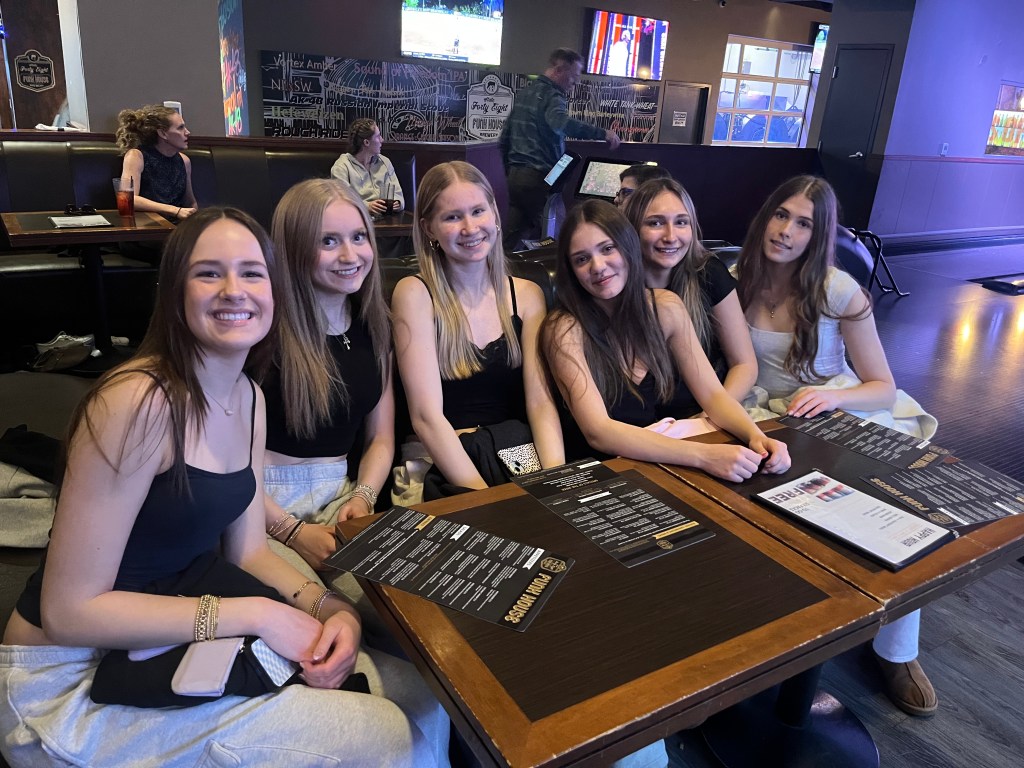 A group of six FEVA teammates sitting together at a restaurant table, smiling and enjoying their time. They are dressed casually, and menus are spread out on the table.