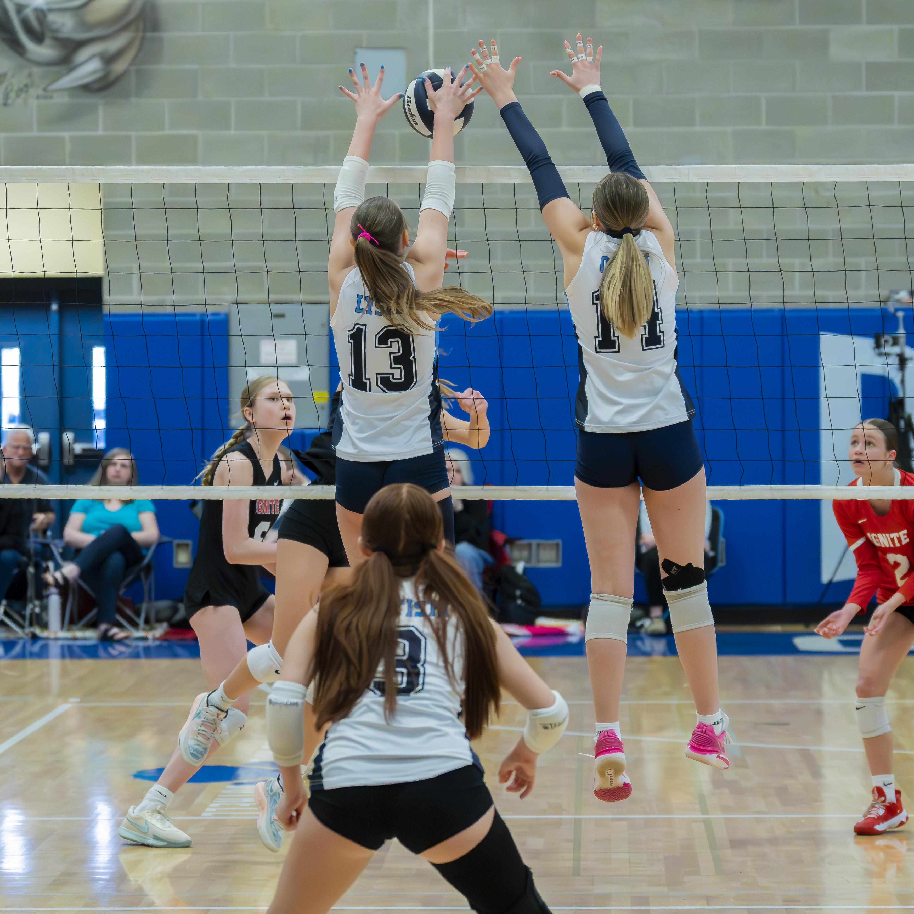 Two volleyball players from the FEVA U15 team jumping to block a hit at Bothell High School during a tournament.
