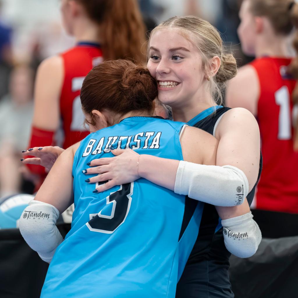 Two FEVA U15 volleyball players embrace joyfully after a match, showcasing camaraderie and celebration.