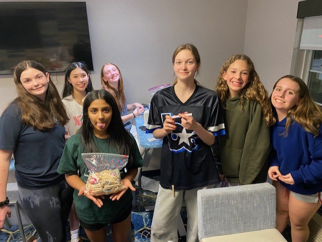 FEVA U14 volleyball team celebrating together in a hotel room, smiling and holding snacks.