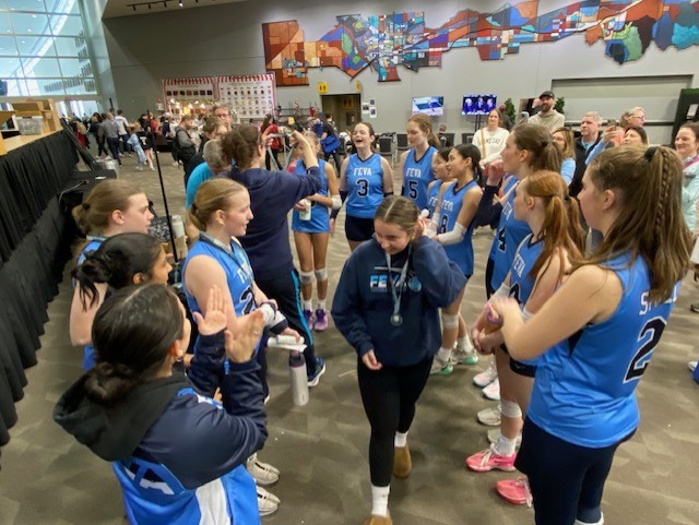 FEVA U14 volleyball team celebrating after a successful tournament, with players in blue uniforms gathering in a cheerful group.