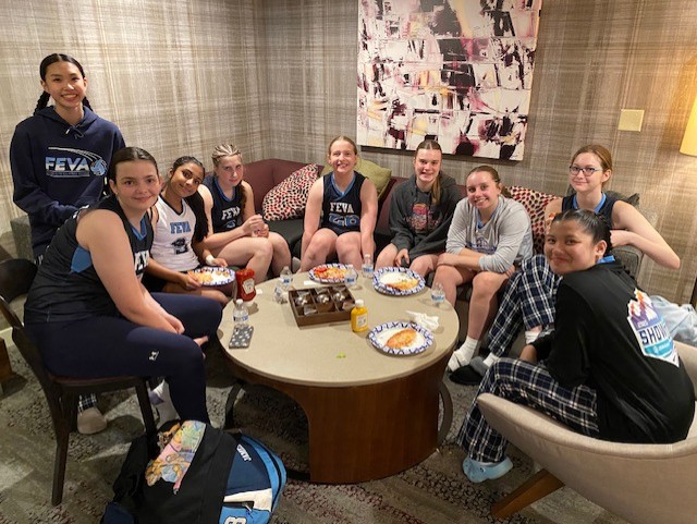 A group of FEVA U14 volleyball players gathering around a table in a cozy room, enjoying snacks and celebrating their season with smiles and team jerseys.