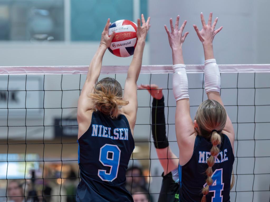 Two volleyball players attempting to block a ball at the net during a match.