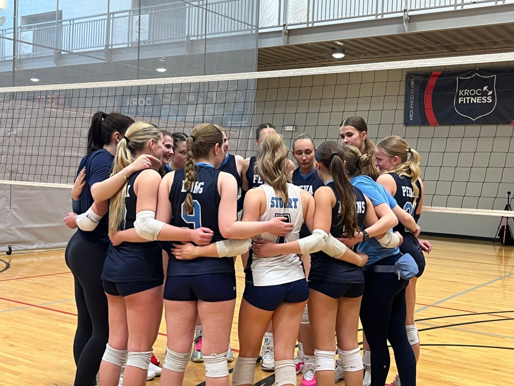 A group of young female volleyball players gathered in a huddle, showing teamwork and camaraderie on the court during practice.
